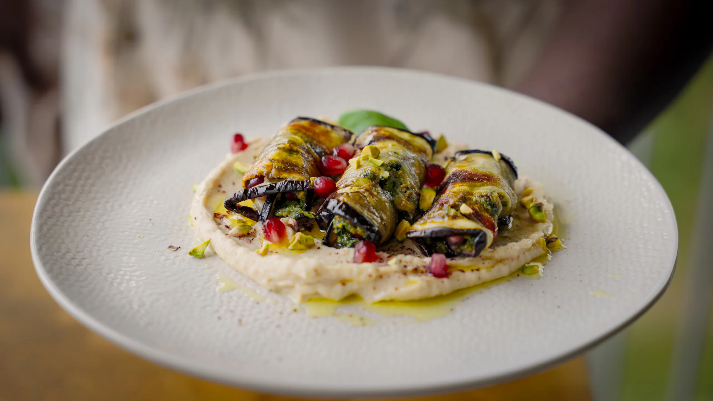 Roasted aubergine rolls filled with pistachio pesto and pomegranate, served with a creamy white bean purée.