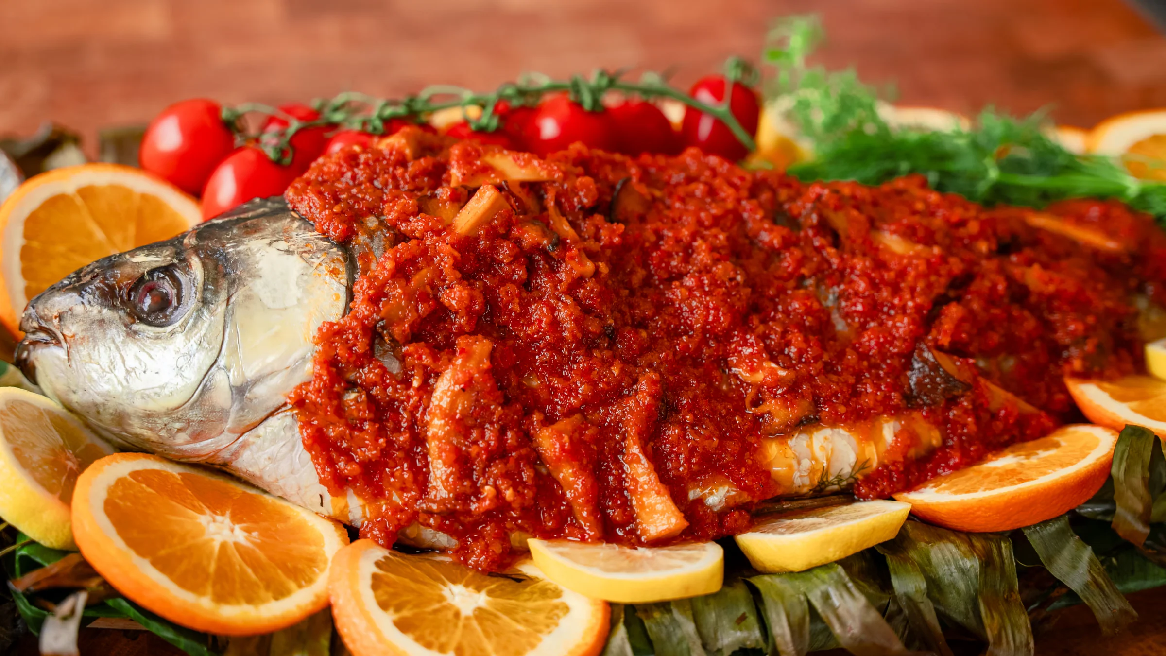 Whole carp in banana leaves with bell pepper and mushrooms sauce.